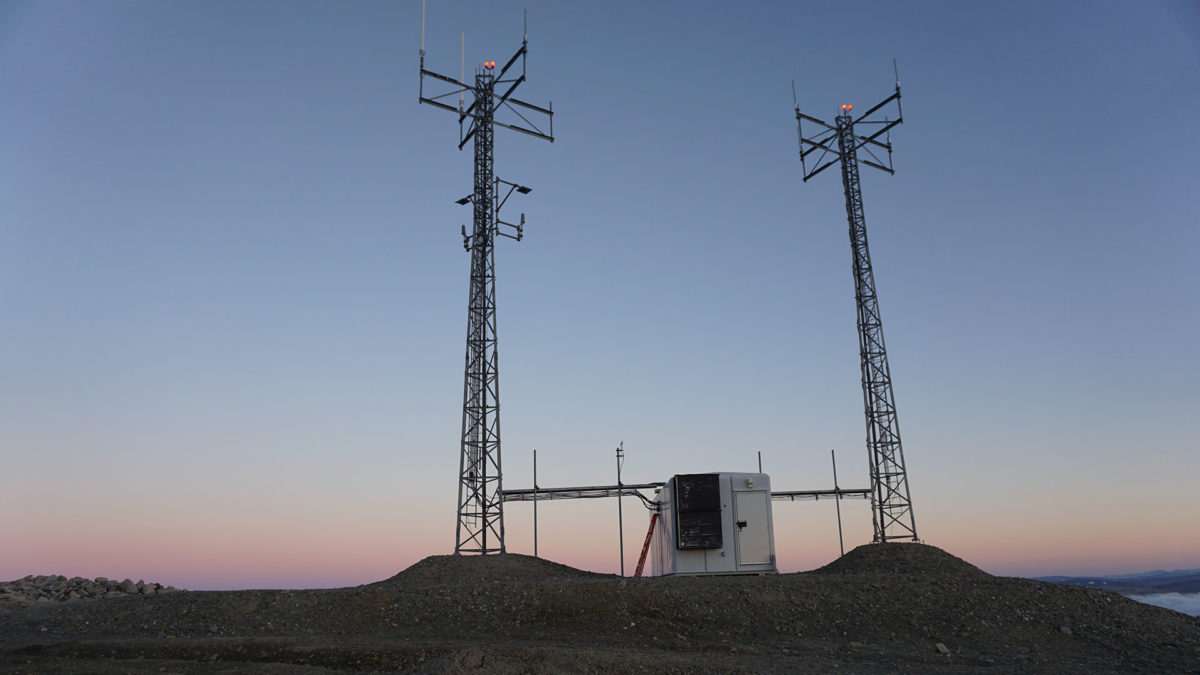 A small structure between two antennas on a rocky terrain at dusk.